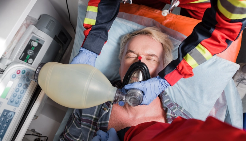 Paramedics using a manual resuscitator and oxygen mask on a patient during a medical emergency.