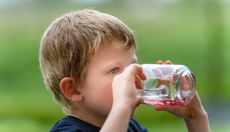 Ένα μικρό παιδί πίνει υγρό από ένα διάφανο ποτήρι σε εξωτερικό χώρο.