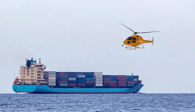 A helicopter approaching a cargo ship in the ocean