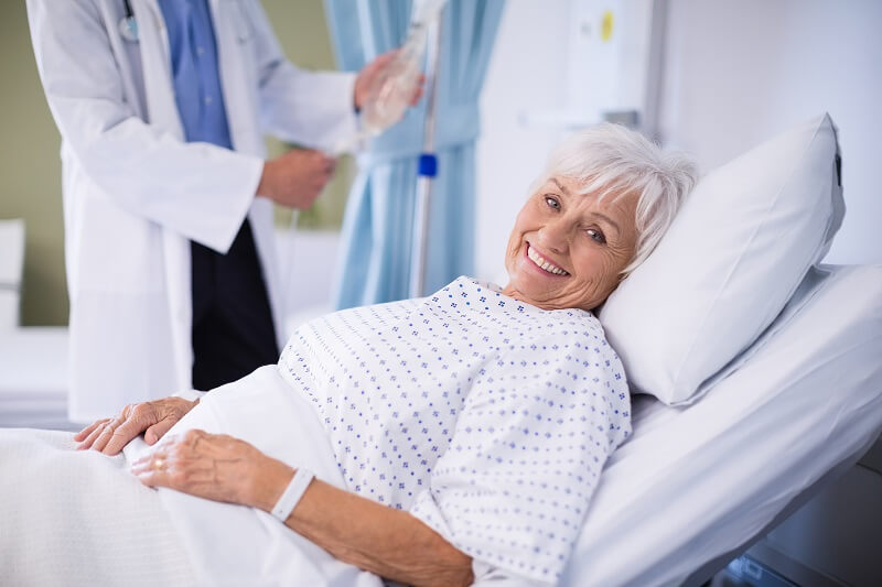Smiling elderly patient in hospital bed with a doctor providing care, symbolizing a smooth transition from hospital to home care.