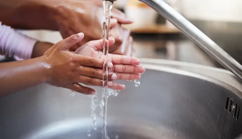 Ένα παιδί πλένει τα χέρια του κάτω από τρεχούμενο νερό με τη βοήθεια ενός ενήλικα.