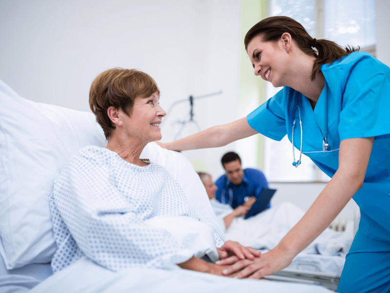 Νοσηλεύτρια φροντίζει χαμογελαστή έναν ασθενή που βρίσκεται σε κρεβάτι νοσοκομείου.