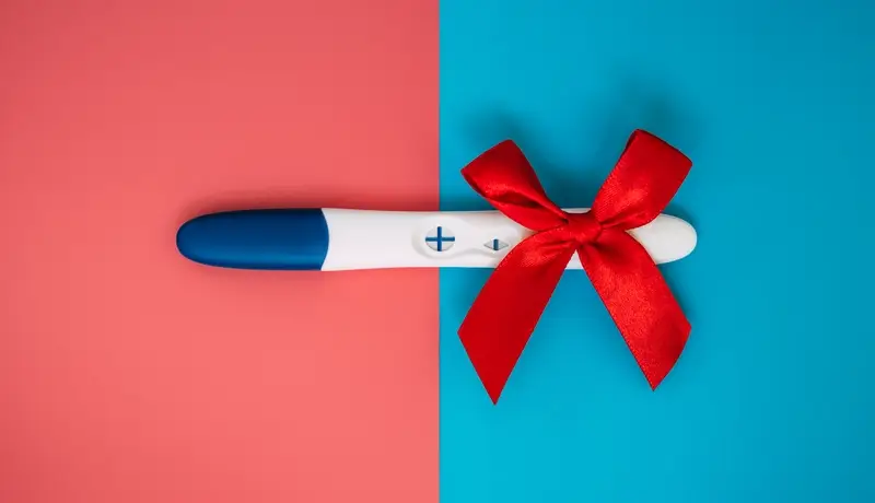 A positive pregnancy test on a pink blue background. A positive pregnancy test result