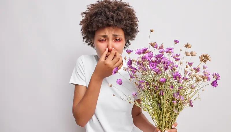 A woman experiencing an allergic reaction to flowers, holding her nose due to sneezing.