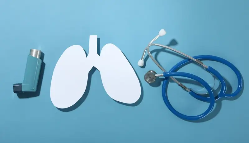 Εισπνευστήρας, διάγραμμα πνευμόνων και στηθοσκόπιο σε μπλε φόντο, που συμβολίζουν την υγεία του αναπνευστικού συστήματος.