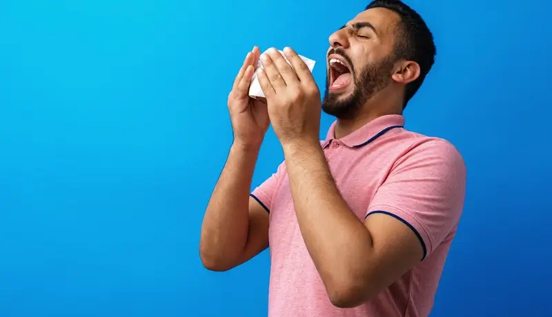 Άντρας που φτερνίζεται, κρατώντας χαρτομάντιλο μπροστά στο στόμα του για να αποτρέψει τη διάδοση μικροβίων.