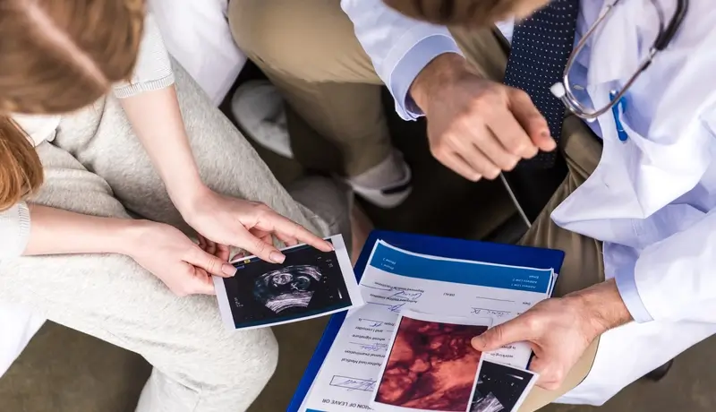 A doctor showing a patient medical images and documents, including an ultrasound scan, as they discuss the results during a consultation.