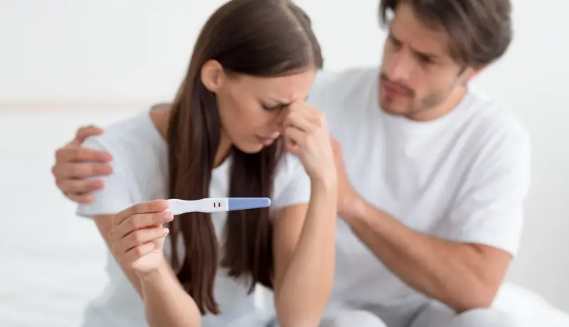 Despaired sad millennial european husband calms, support his wife, lady hold pregnancy test