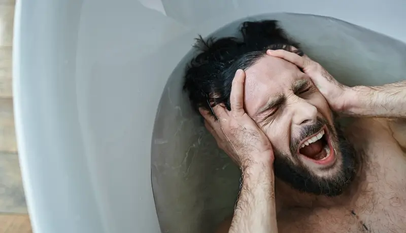 Άντρας σε μπανιέρα κρατώντας το κεφάλι του με τα χέρια του, ουρλιάζοντας από πόνο ή απογοήτευση.