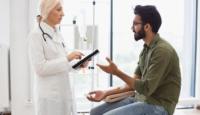 Doctor consulting with a patient receiving intravenous treatment in a clinical setting.