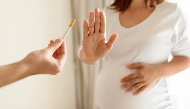 Pregnant woman rejecting a cigarette offered to her, holding up her hand to say no.