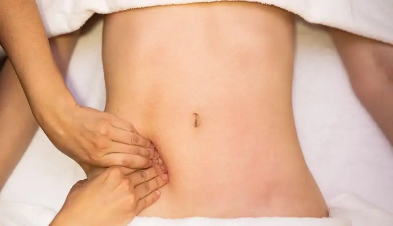 A medical professional performing a gentle abdominal examination on a female patient to check for signs of pelvic inflammatory disease.