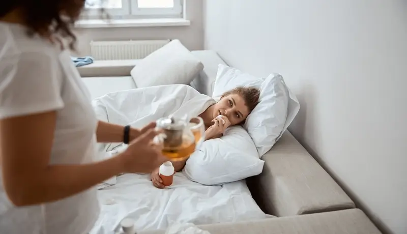 Ασθενής ξαπλωμένη στον καναπέ με ζεστό ρόφημα και φροντίδα