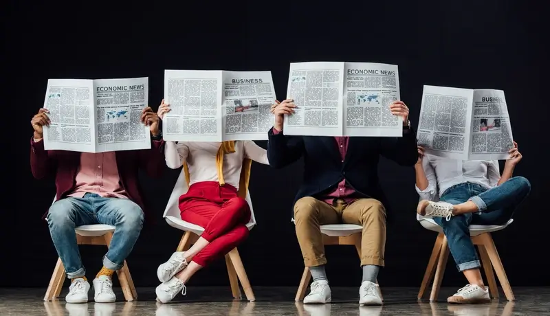 group of casual businesspeople with obscure faces sitting on chairs and reading business newspapers