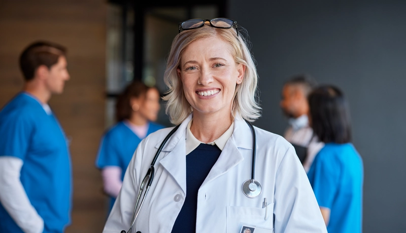Γυναίκα γιατρός με στηθοσκόπιο χαμογελάει, με φόντο ιατρικό προσωπικό.