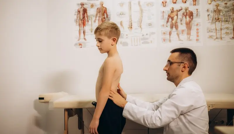 Orthopedic doctor examining a child's back in a clinic.