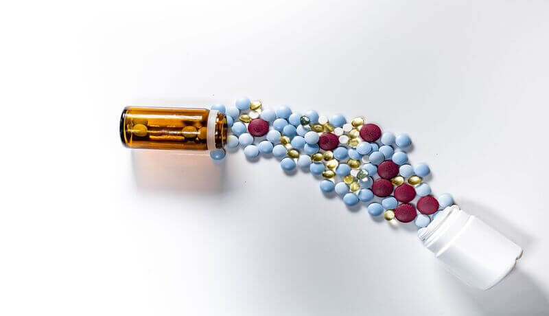 Top view of several colorful pills spilling from a glass and plastic bottles on a white background