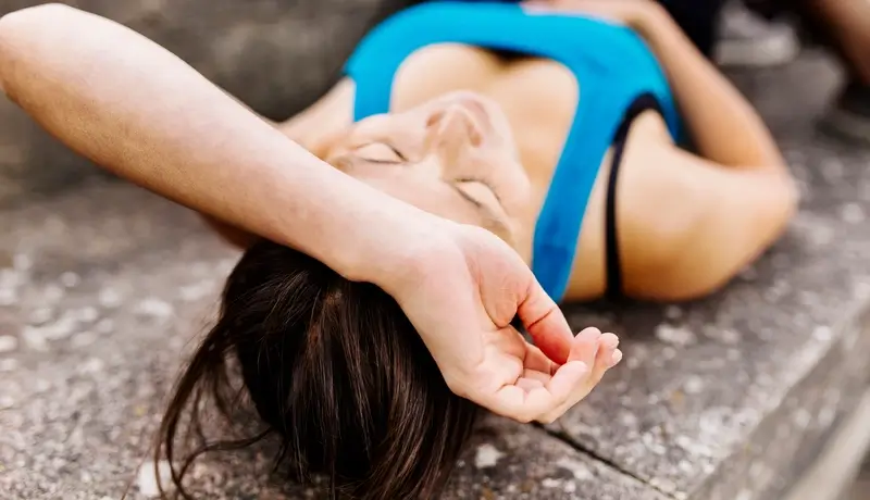 Woman lying outdoors, appearing unconscious, potentially experiencing a seizure, wearing a sports tank top.
